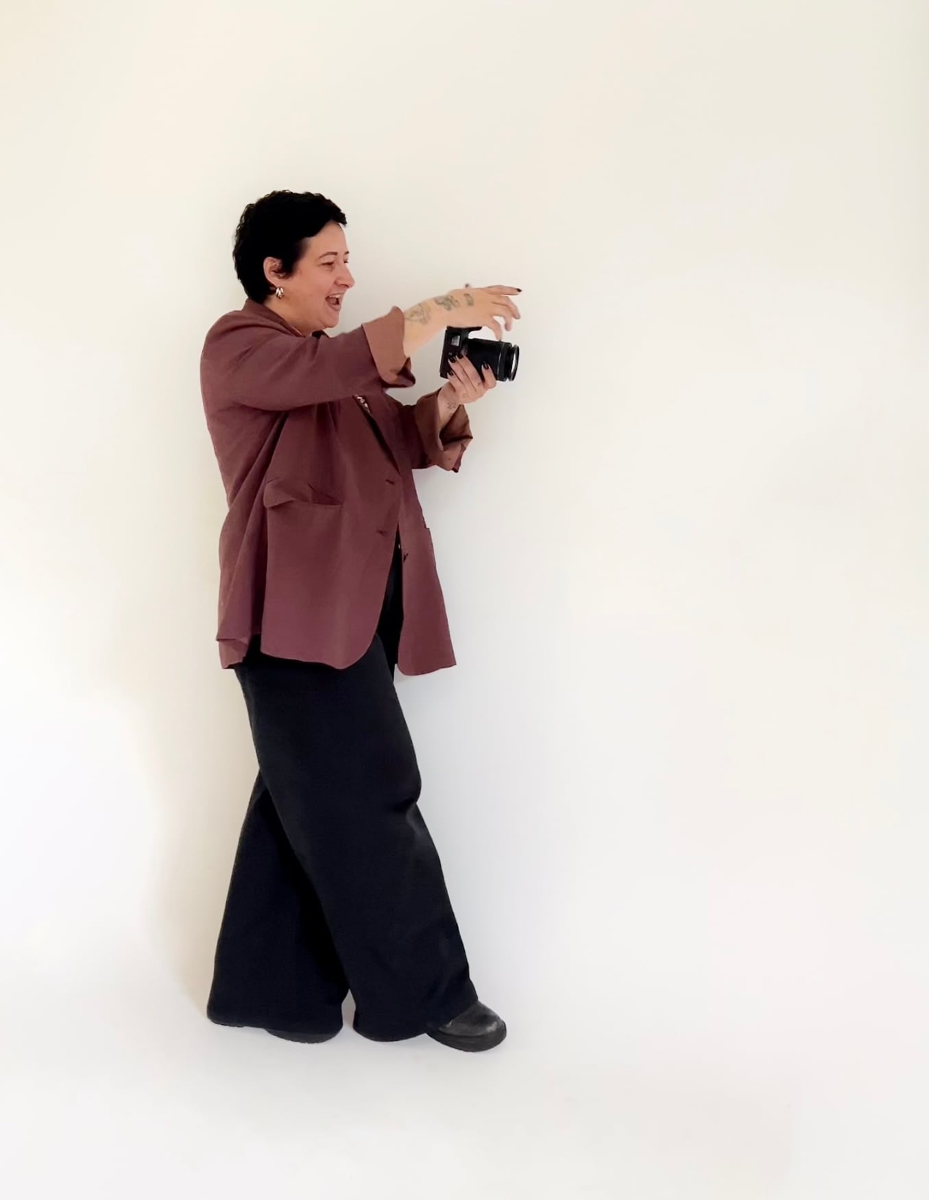 Evelyn Rodrigues fotografando, de blazer vinho, em fundo claro de estúdio